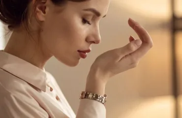 Elitna zhinocha parfumeriya shcho robyt aromat po-spravzhnomu unikalnym Close-up profile of a woman examining her hand and nails, wearing a beige blouse and a metal watch in warm indoor lighting.