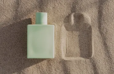 Parfumy na lito yak obraty aromat yakyy ne vtomlyuye u speku Mint-green rectangular bottle on beach sand with a square imprint nearby.