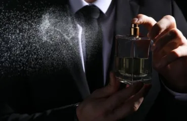 Suchasni trendy v cholovichiy parfumeriyi Man in a suit sprays perfume from a square glass bottle, mist billowing to the left.