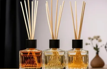 Aromadyfuzor z aromatom ulyublenykh parfumiv stylnyy aromat dlya domu Three square glass reed diffuser bottles with black caps and tall wooden reeds, on a wooden surface.