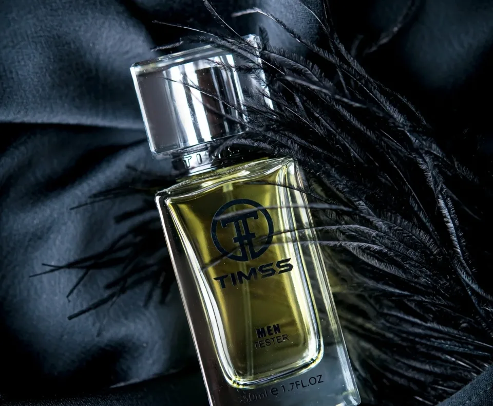 Cologne bottle labeled TIMSS, yellow liquid, on black fabric with black feathers in the background (men's tester).
