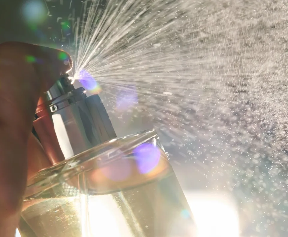 Close-up of a hand holding a small torch, sparks spraying toward a glass of champagne in a dim setting.